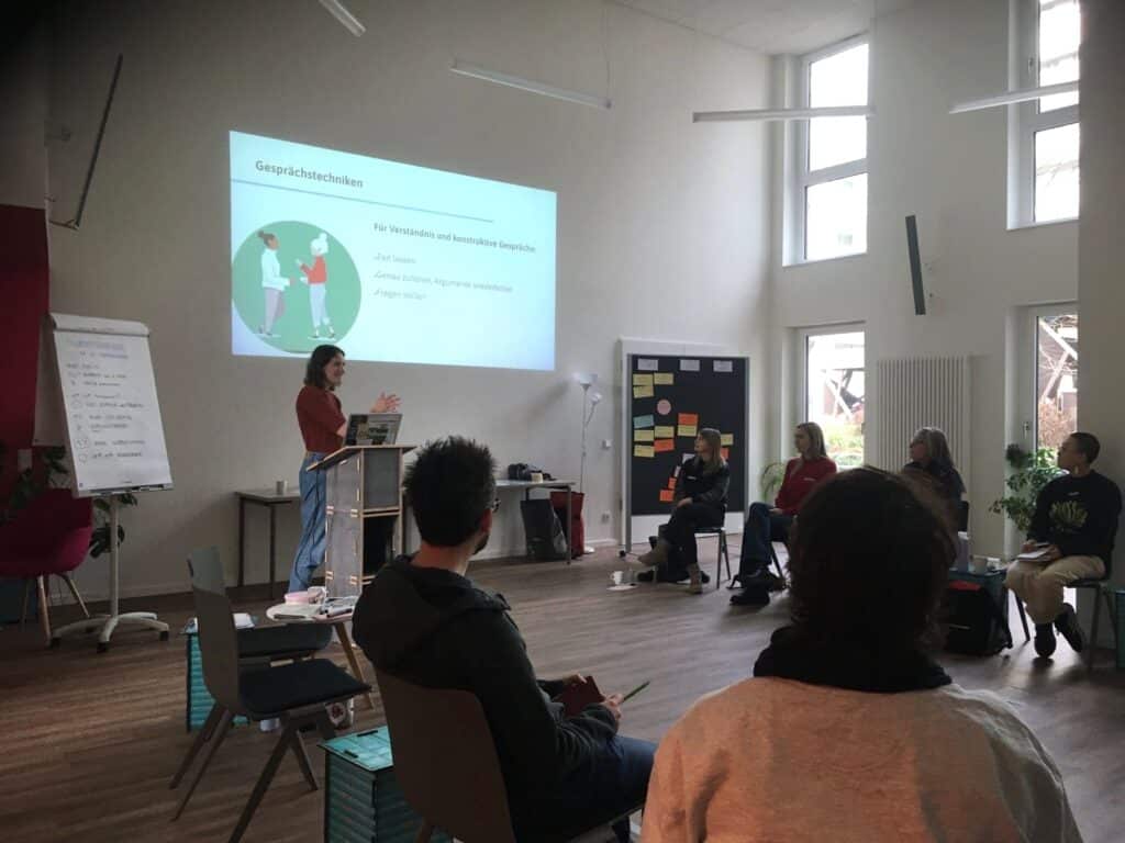 Eine Gruppe Menschen hört einer Referentin bei einem Workshop zu.